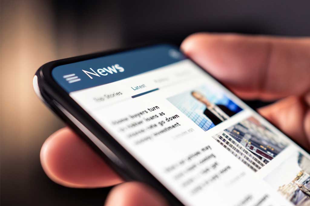 A hand holding a phone with the news feed on the screen.